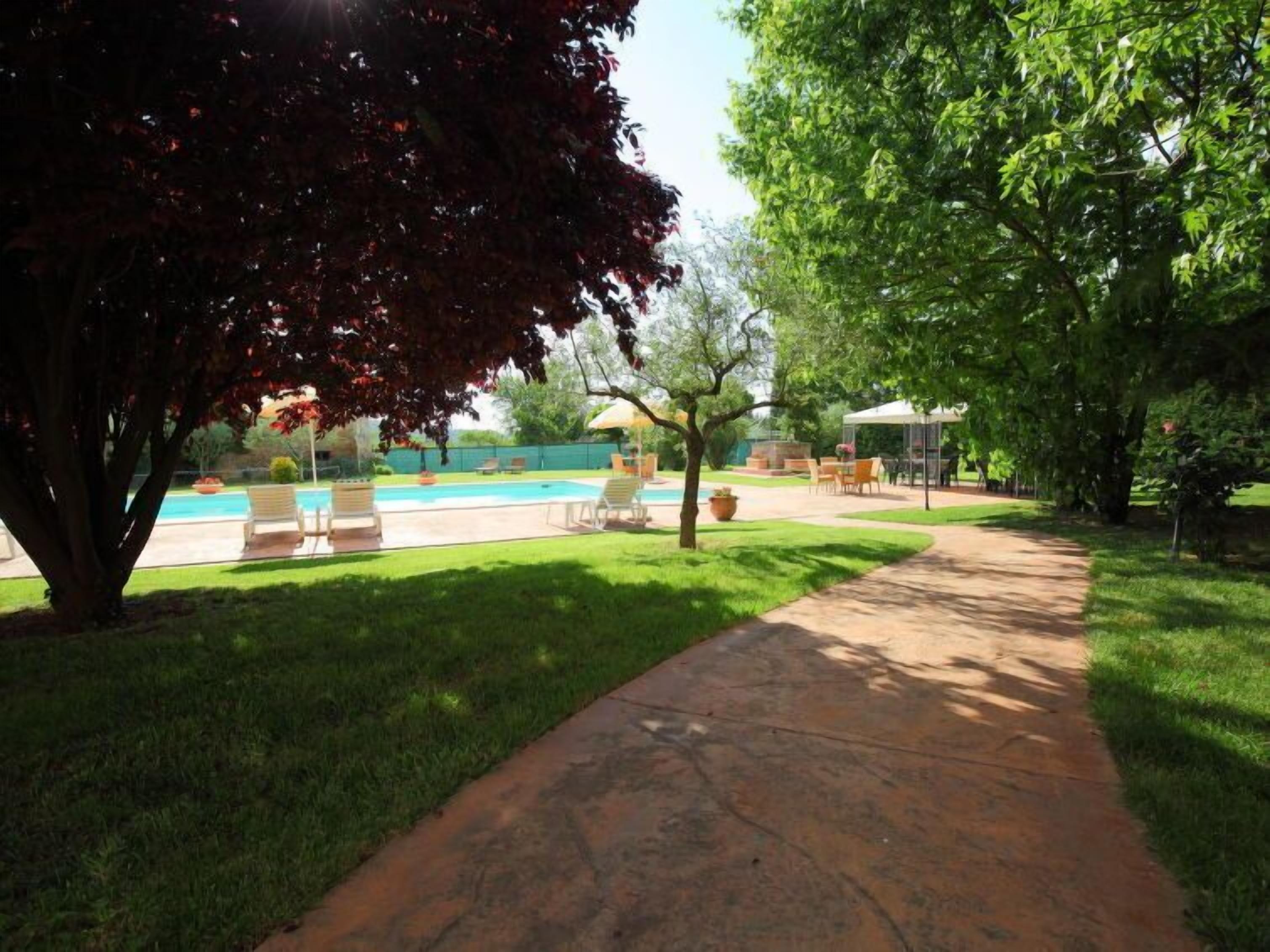 A backyard with a swimming pool, a covered patio, and a paved walkway.