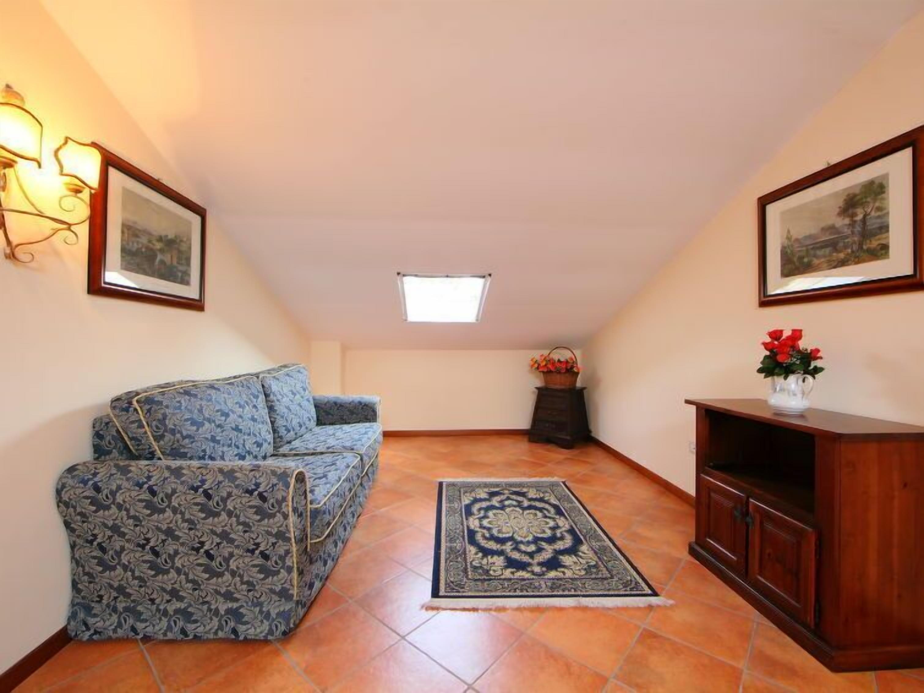 A small, cozy room with a blue patterned sofa, a wooden cabinet, a rug, and two framed pictures on the walls.