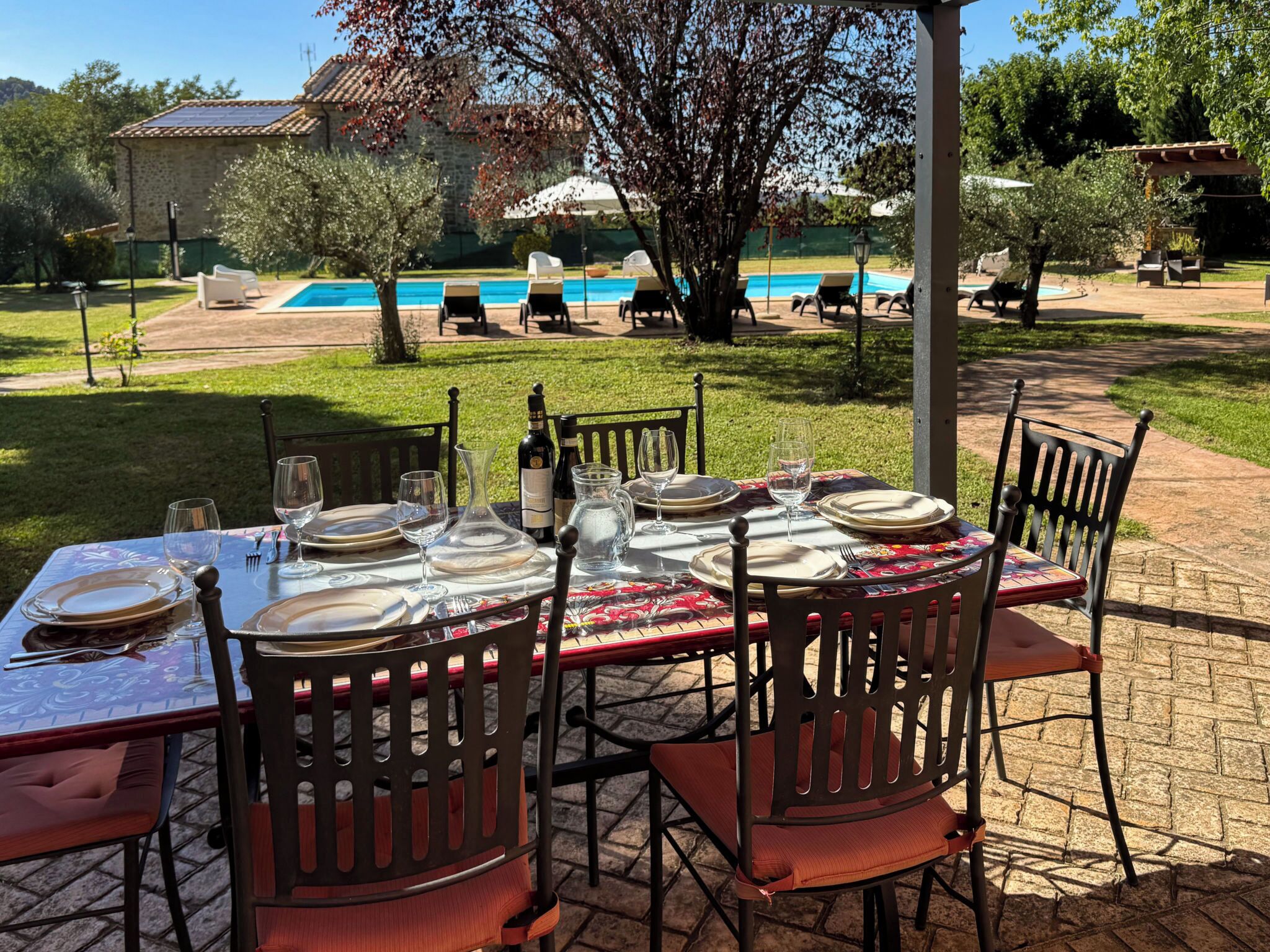 Un espacio al aire libre para comer con una mesa preparada para seis personas, sillas alrededor y una piscina al fondo.