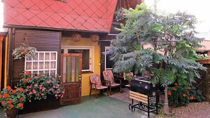 A traditional house with a red roof, a wooden door, and a small window. There is a bench and a grill outside.