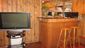 A bar area with a television, bar stools, and shelves with glasses and bottles.