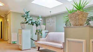 A hallway with a light-colored sofa, a chandelier, and potted plants. - Sun Palace Wellness Hotel Marianske Lazne (Marianske Lazne)