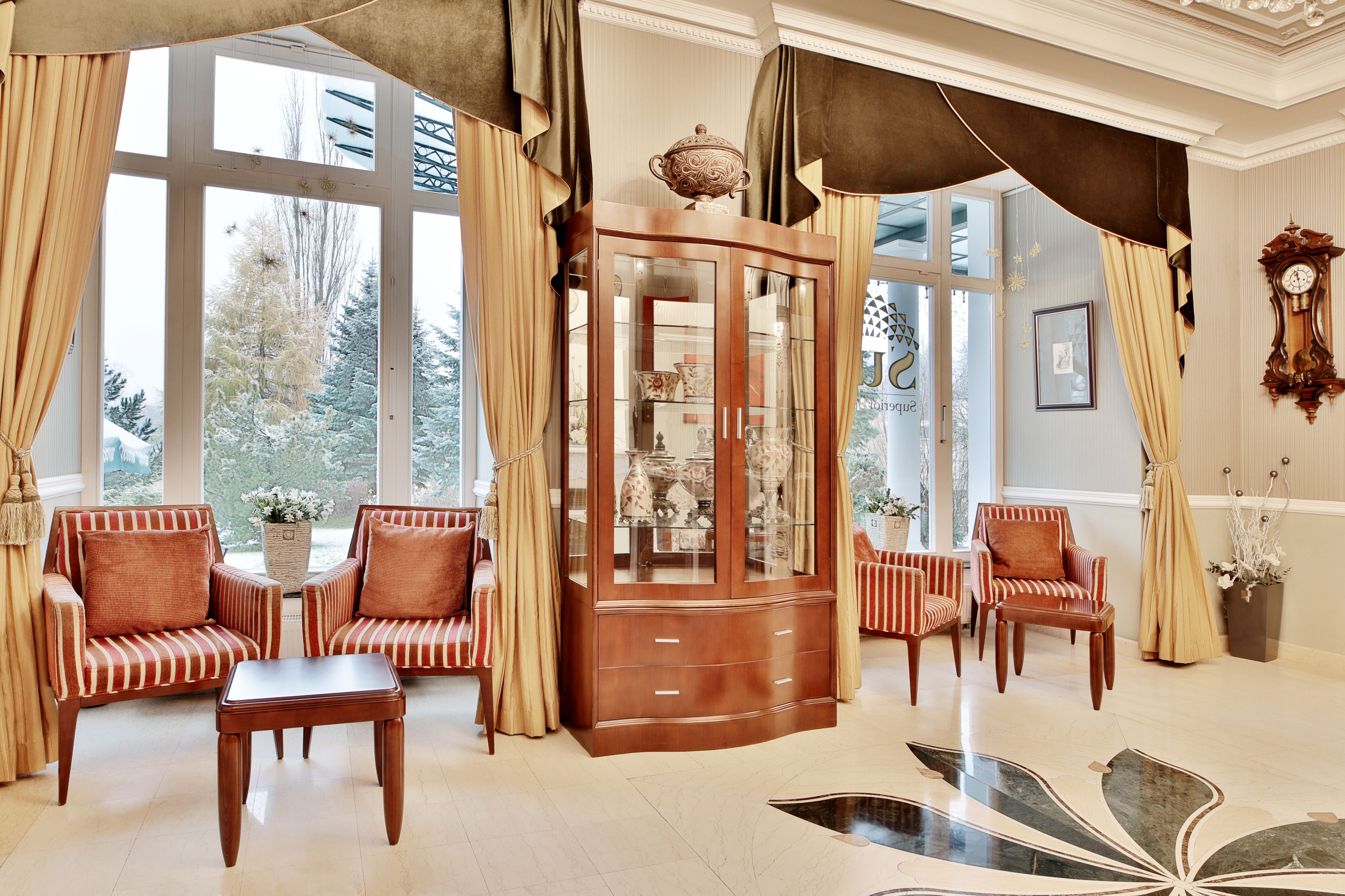 A room with a large window, a wooden cabinet with glass doors, striped armchairs, and a table.