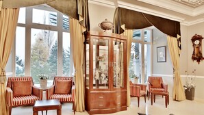 A room with a large window, a wooden cabinet with glass doors, striped armchairs, and a table. - Sun Palace Wellness Hotel Marianske Lazne (Marianske Lazne)
