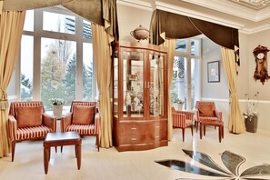 A room with a large window, a wooden cabinet with glass doors, striped armchairs, and a table. - Sun Palace Wellness Hotel Marianske Lazne (Marianske Lazne)