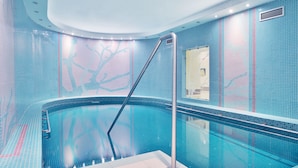 A modern indoor swimming pool with a curved design, tiled walls, and a central column. - Sun Palace Wellness Hotel Marianske Lazne (Marianske Lazne)