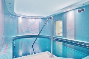 A modern indoor swimming pool with a curved design, tiled walls, and a central column. - Sun Palace Wellness Hotel Marianske Lazne (Marianske Lazne)