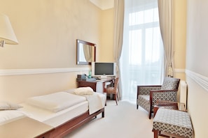 A hotel room with a bed, a desk with a computer, a TV, and two chairs.