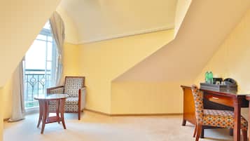 A room with a sloped ceiling, a balcony with a wrought iron railing, two wooden chairs with patterned upholstery, and a small round table.
