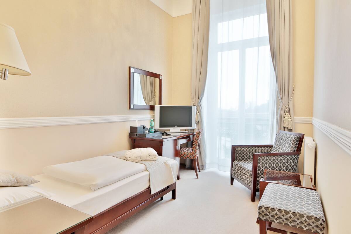 Ein Hotelzimmer mit einem Bett, einem Schreibtisch mit Computer, einem Fernseher und zwei Stühlen.