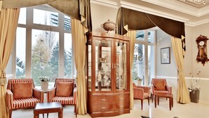 A spacious room with large windows, a wooden cabinet, striped armchairs, and a small table.