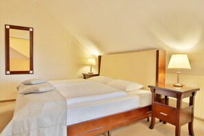 A neatly made bed with pillows and a blanket, a bedside table with a lamp, and a mirror on the wall. - Sun Palace Wellness Hotel Marianske Lazne (Marianske Lazne)