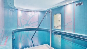 A modern indoor swimming pool with a curved design, tiled walls, and a central column.