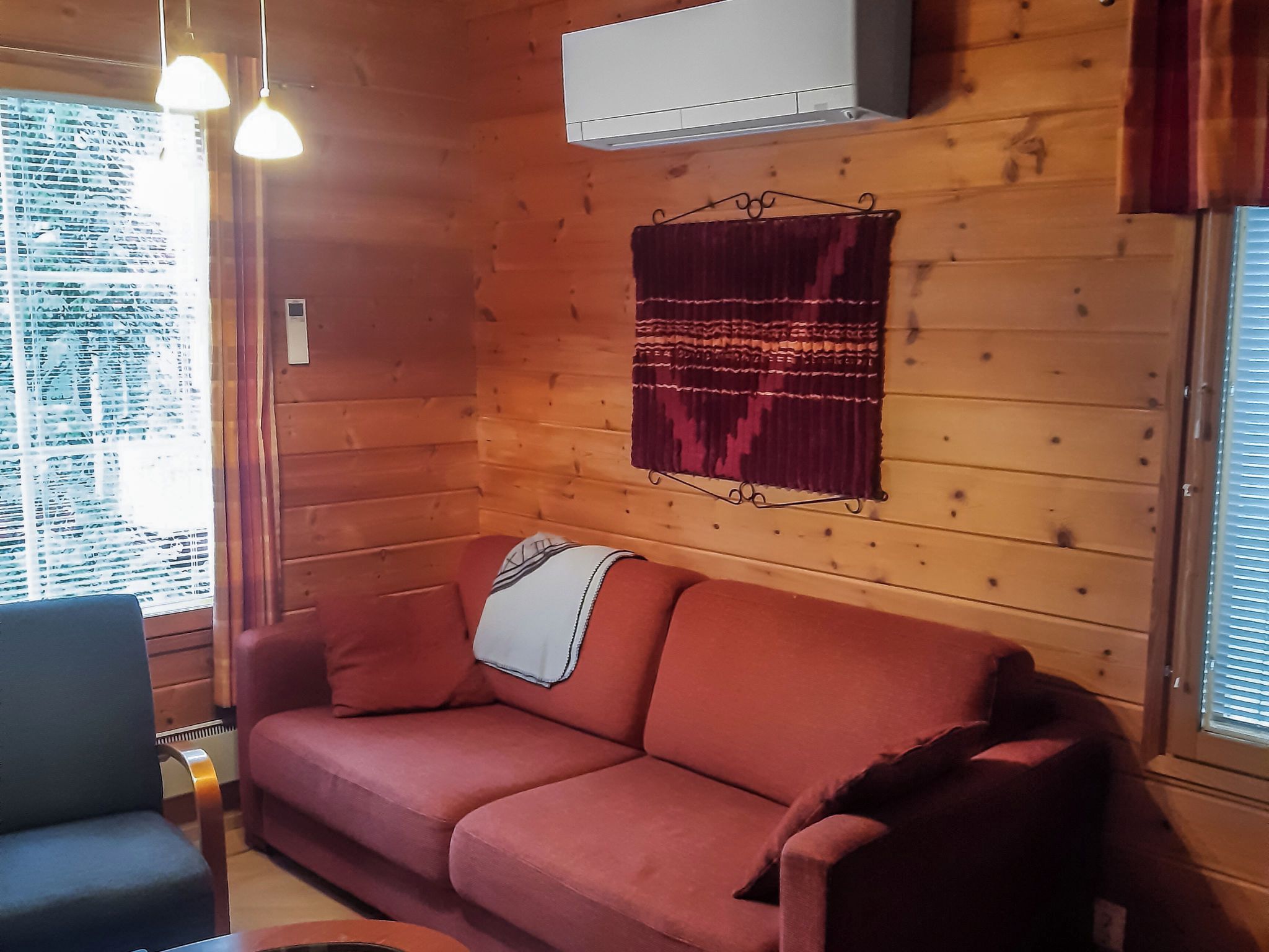 Ein Holzblockhaus-Interieur mit einem roten Sofa, einem kleinen Tisch und einem Fenster mit Rollläden.
