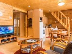 A cozy wooden cabin interior with a dining area, kitchen, and a TV on a wooden stand.