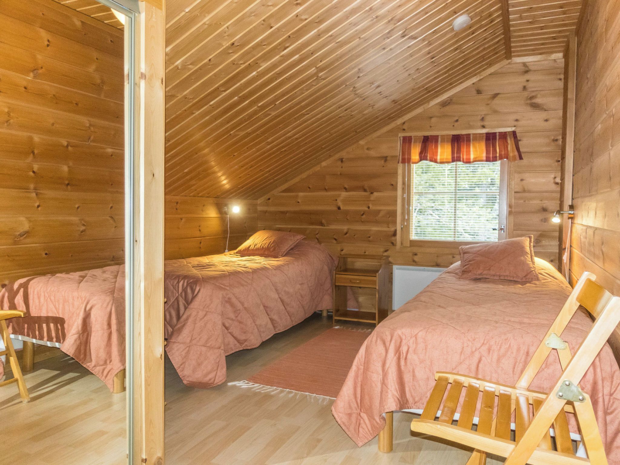 Un dormitorio acogedor en el ático con dos camas, una ventana con persianas y una escalera de madera.