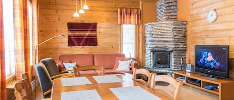 L’intérieur chaleureux d’un chalet avec une cheminée en pierre, une table à manger avec des chaises, un canapé et un téléviseur.
