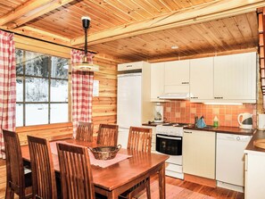 Ein Holzinterieur mit Esstisch, Stühlen, einem Kühlschrank, einem Herd und einem Fenster mit Vorhängen.