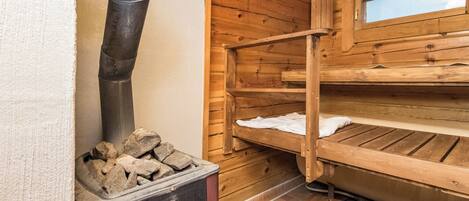 A sauna with wooden benches, a stone heater, and a blue basin.