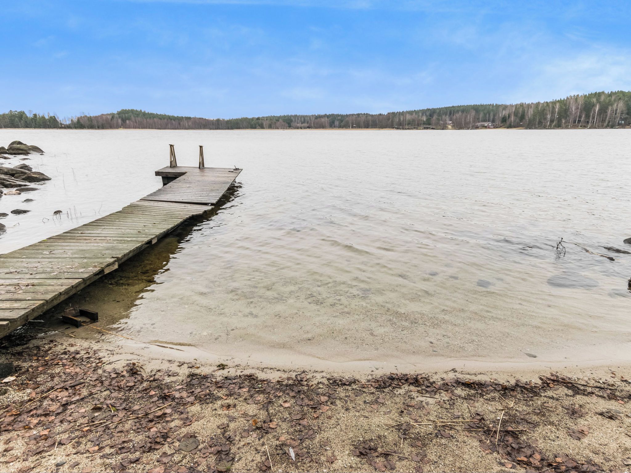 A wooden dock extending into a calm body of water with a forested hill in the background.