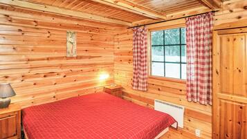 Une chambre dans un chalet en bois, avec un lit, une table de chevet, une lampe, une fenêtre avec des rideaux et un radiateur.