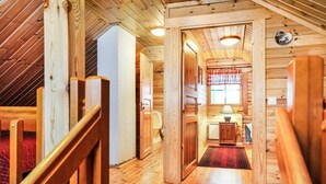 Een houten interieur met een trap, een klein keukenhoekje en een raam met gordijnen.