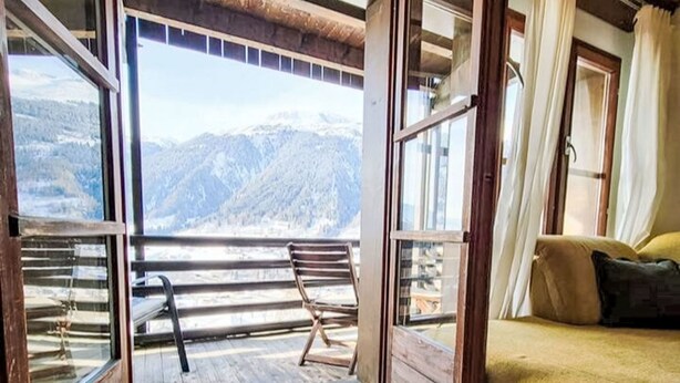 A room with a large sliding glass door leading to a balcony with a mountain view.
