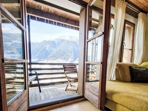 Una habitación con un amplio ventanal corredera que da a un balcón con vistas a la montaña.