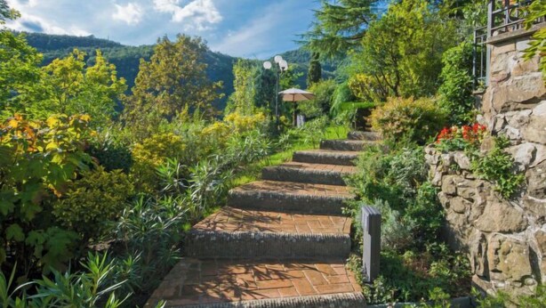 Un escalier en pierre menant au sommet d’une colline, entouré d’une végétation luxuriante et avec une montagne en arrière-plan.