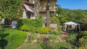 Une maison traditionnelle dotée d’un balcon, entourée d’une végétation luxuriante et surplombant un ciel d’un bleu limpide.