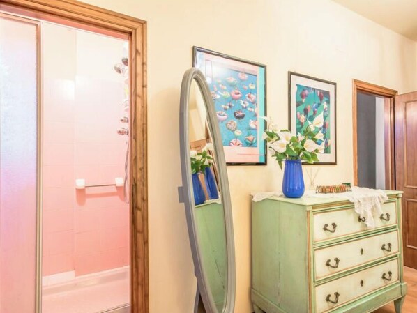 Een badkamer met een douche, een wastafel met spiegel en twee kunstwerken in lijsten aan de muur.