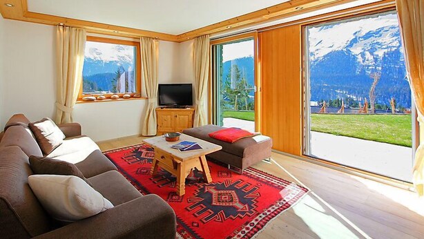 A living room with a sofa, a coffee table, and a TV. There are large windows with a mountain view. - Chesa Sül Muot by Interhome (St. Moritz)