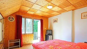 A bedroom with a wooden ceiling, a bed with a floral bedspread, a television on a dresser, and a window with curtains.