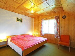 A wooden cabin room with a bed, a chair, and a window with curtains.
