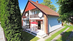 A two-story house with a red roof, a balcony, and a small patio with a table and chairs.