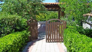 Ein Weg führt zu einer Holzw pergola mit einem Ziegeldach, umgeben von üppigem Grün.