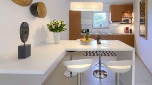 A modern kitchen with a central island, white bar stools, a hanging light fixture, and wooden wall decor. - Sv. Ivan 1 by Interhome (Umag)