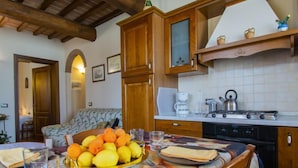 A cozy kitchen with wooden cabinets, a dining table set with plates, glasses, and a fruit basket. - Leonardo - Borgo Fontana by Interhome (Vinci)