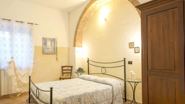 A bedroom with a bed, a wooden wardrobe, a small table, and a chair.