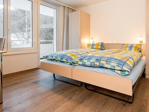 A modern bedroom with a bed, wooden flooring, a window with a view, and a nightstand.