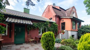 A two-story house with a green door, a patio with a table and chairs, and a garden with various plants and flowers. - Apartment Rekowo by Interhome (Rekowo)