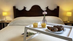 Ein ordentlich bezogenes Bett mit einem Tablett, auf dem zwei Orangensäfte, eine kleine Vase mit einer Blume und ein Teller mit Croissants stehen.
