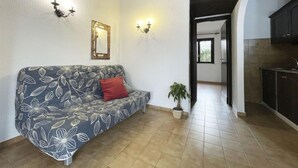 Ein Wohnzimmer mit einer Couch, einer Topfpflanze und Blick in die Küche.