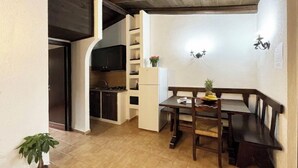 Eine kompakte Küche mit dunklen Schränken, einem weißen Kühlschrank und einem Essbereich mit Holztisch und Bank.