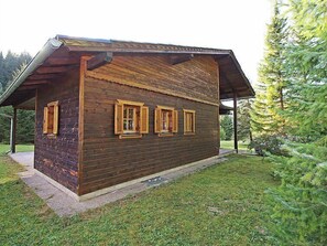 A rustic wooden cabin with a sloped roof, three windows with shutters, and a covered porch area.