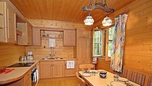 L’intérieur d’un chalet en bois comprend une cuisine, un coin repas et une fenêtre avec des rideaux.