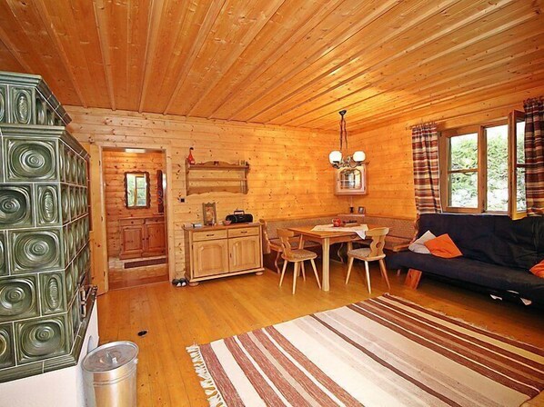 A cozy cabin interior with a wooden ceiling, a dining area with a table and chairs, a sofa, and a kitchen area with cabinets and a sink.