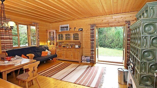 L’intérieur chaleureux d’un chalet avec un plancher en bois, un canapé, une table à manger et un coin cuisine équipé de placards et d’une cuisinière.