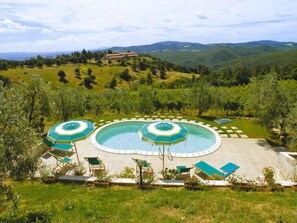 A circular pool with two umbrellas, surrounded by lounge chairs and a view of rolling hills. - Cielo Terra by Interhome (Gambassi Terme)