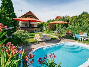 A swimming pool with lounge chairs and umbrellas, surrounded by a garden and a house with a balcony. - Flamingo by Interhome (Balatonalmadi)